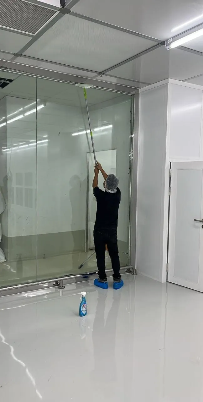 Technician pole-cleaning a cleanroom glass partition and ceiling