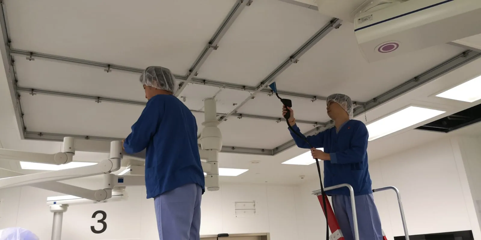 Technicians scanning a ceiling HEPA filter with a probe during a leak test
